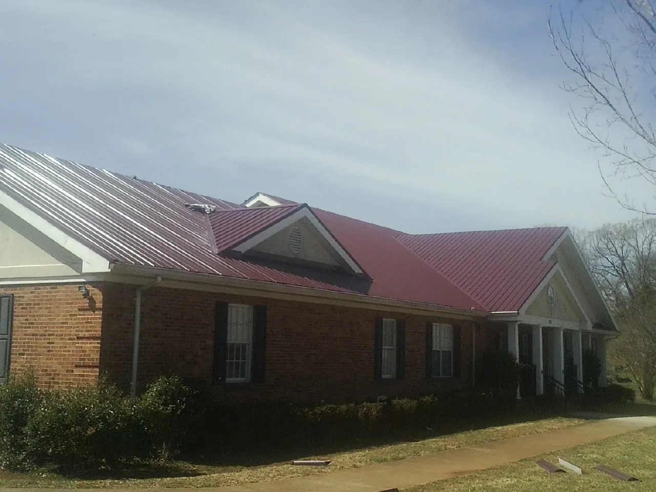 Red metal roof with gabled entries on a long brick building, from a Hail Damage Roof Repair job in Bradenton