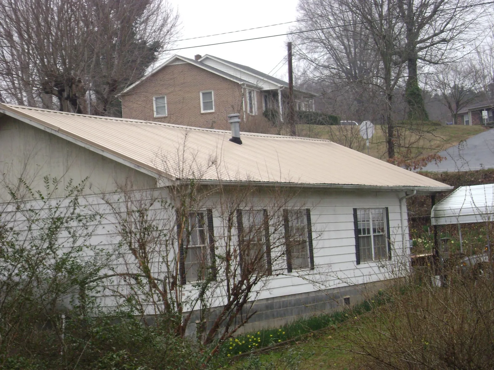Tan metal roof on a white sided house set into a hillside — Commercial Roofing by Roofing Brothers in Bradenton